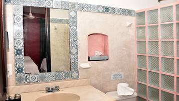 Un baño con lavamanos, espejo, inodoro y mampara de vidrio.