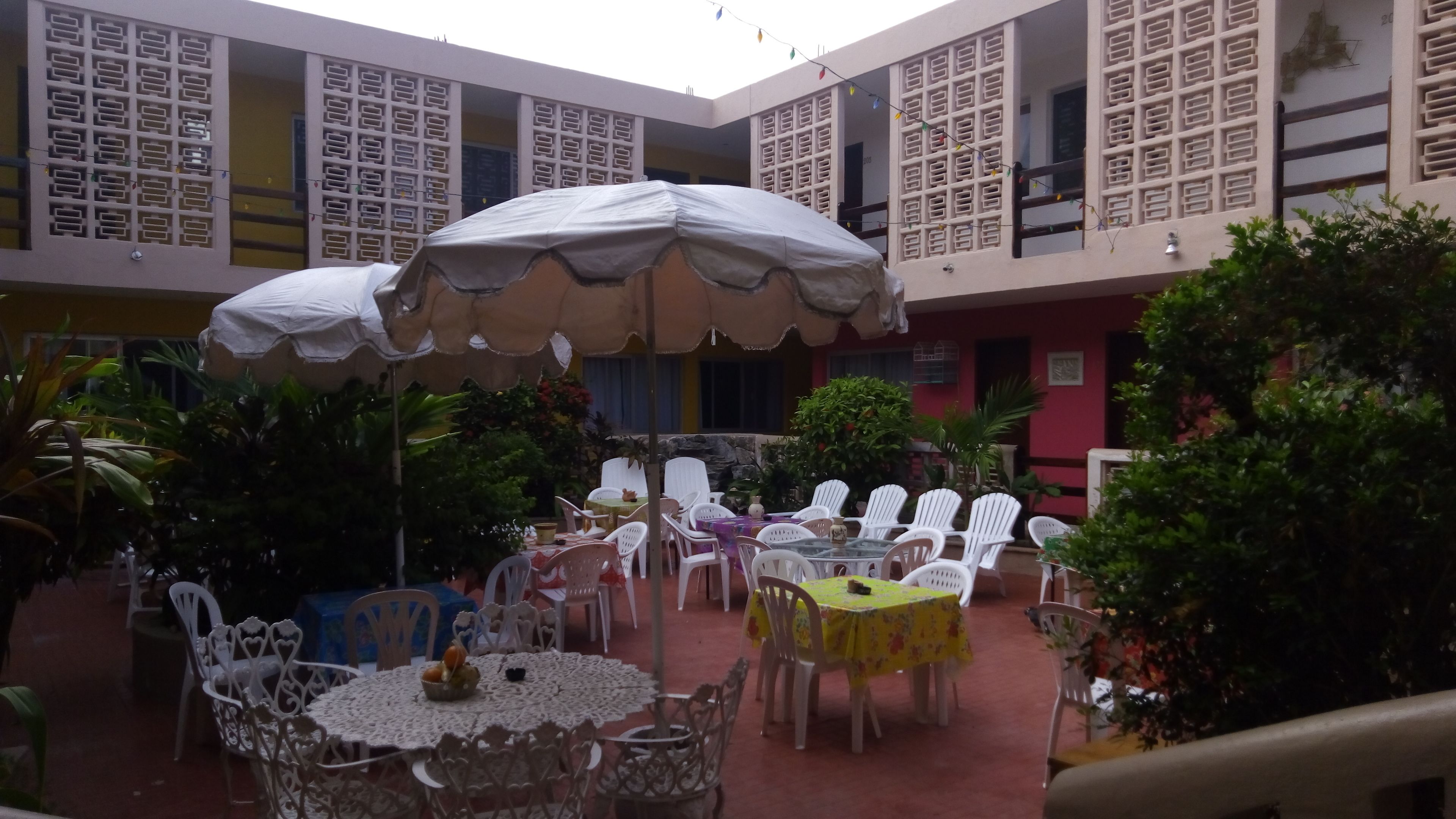 Un área de comedor al aire libre con mesas y sillas, cubierta por sombrillas y rodeada de follaje.