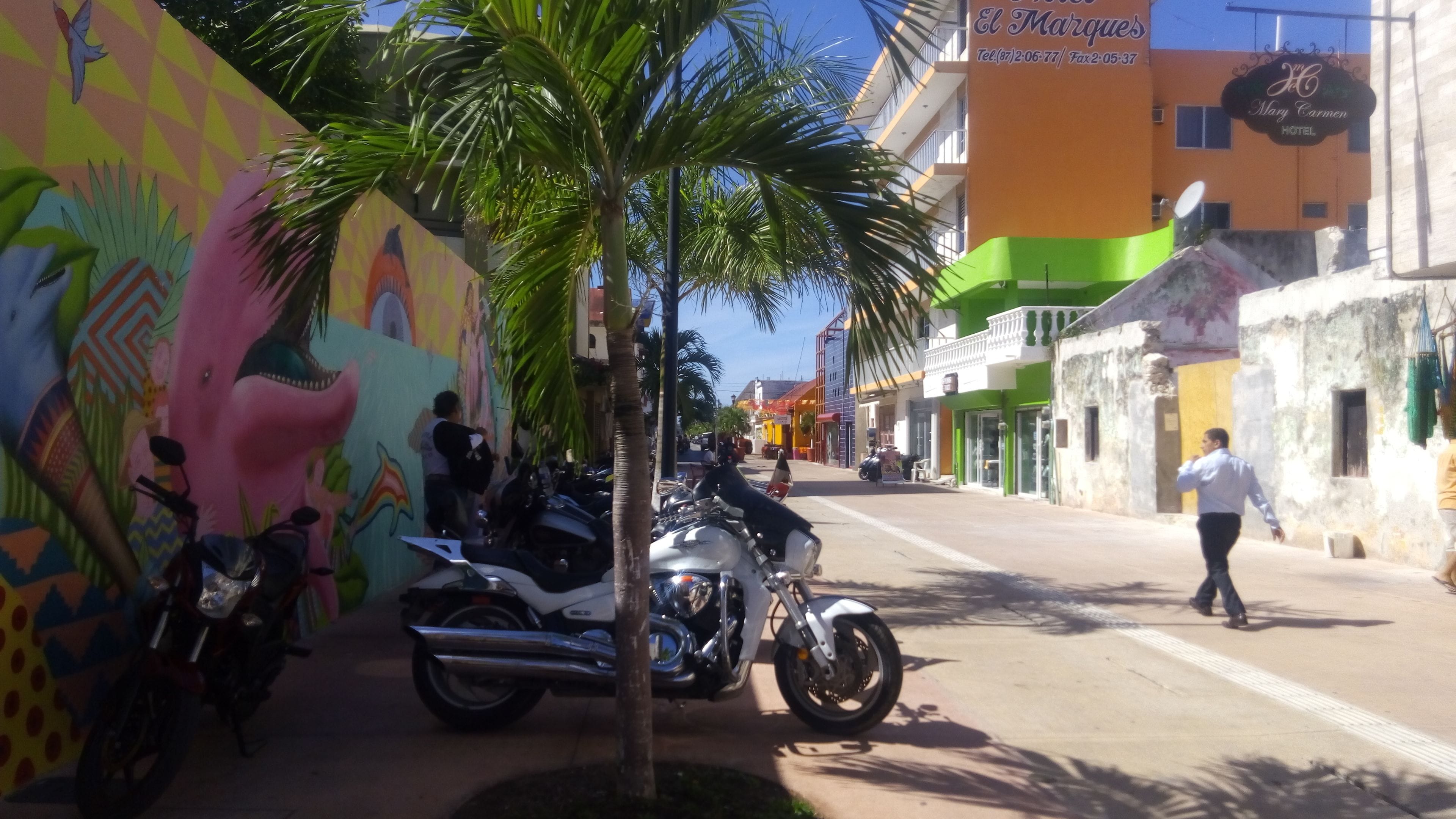 Calle con edificios coloridos, un mural y motocicletas estacionadas.