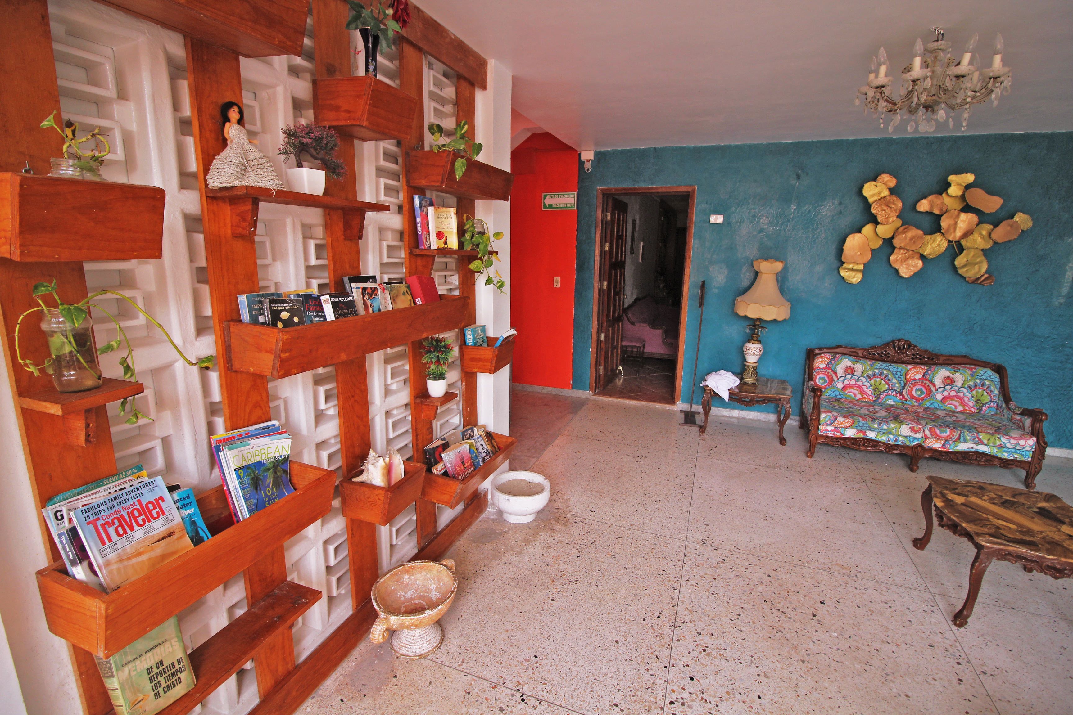 Een woonkamer met een houten boekenkast, een kleurrijke bank, een kroonluchter en een blauwe wand.
