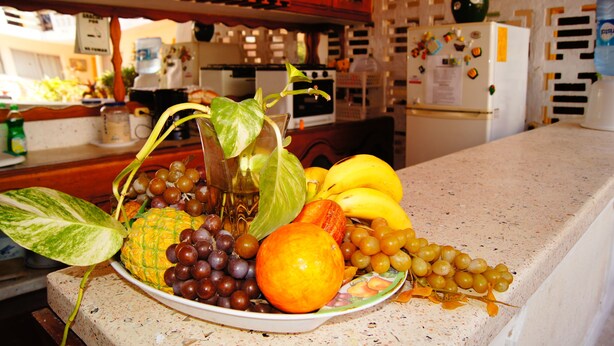 Uma bancada de cozinha com uma fruteira contendo uvas, uma laranja e bananas.