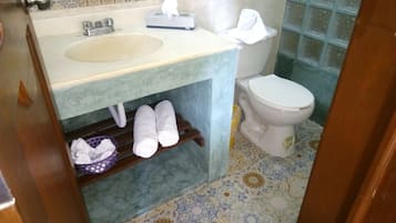 A bathroom with a sink, toilet, and a shelf with towels.