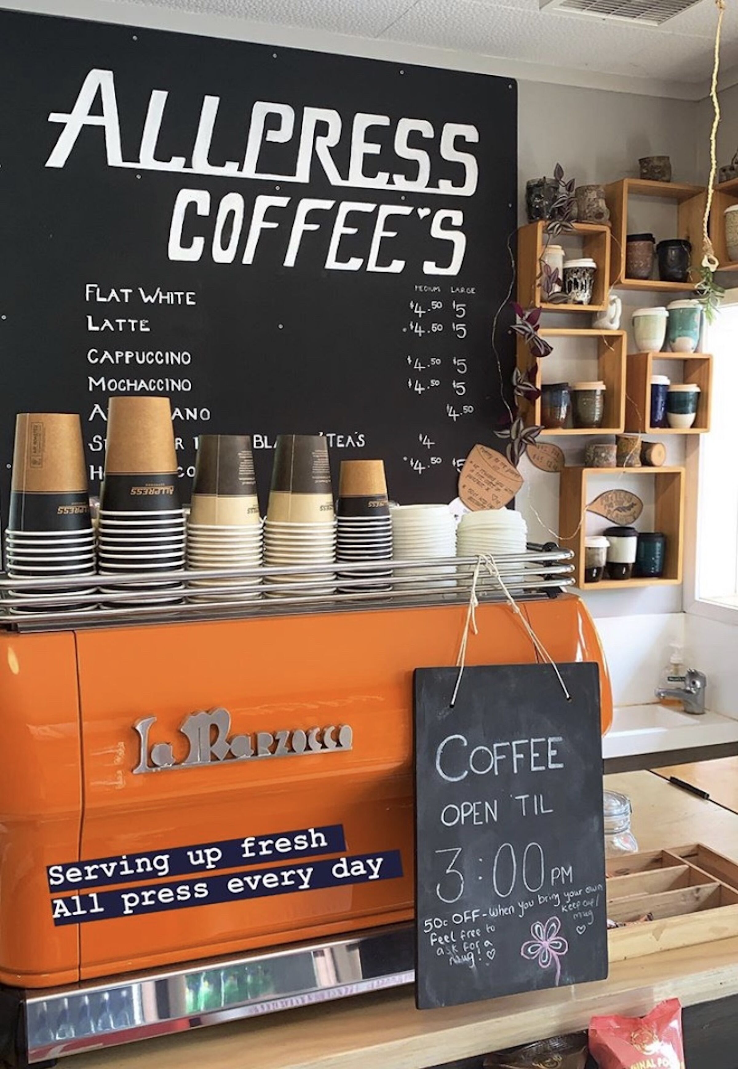 A coffee shop with a menu board listing flat white, latte, cappuccino, mocha, and macchiato. A sign indicates the shop is open until 3:00 PM.
