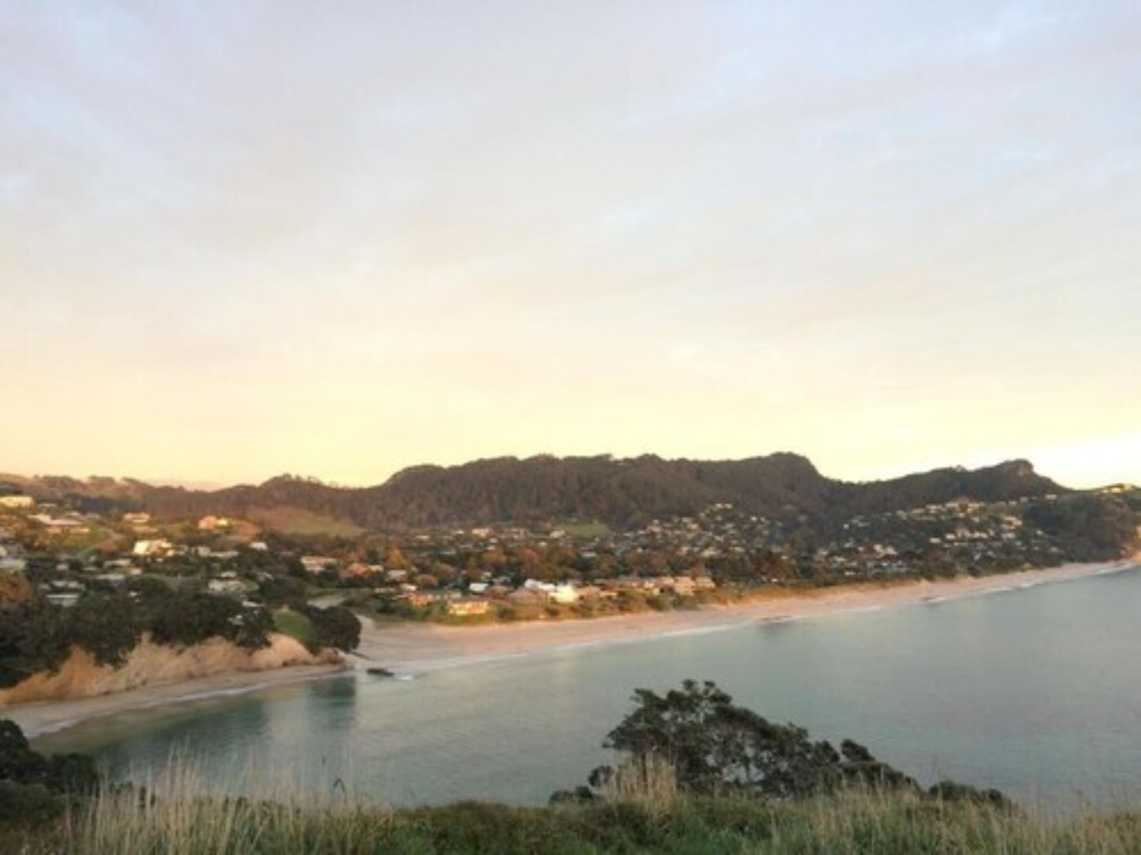 A coastal landscape with a beach, houses, and hills in the background.