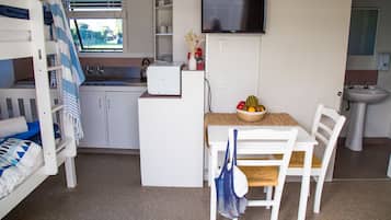 Ett litet rum med våningssängar, ett minikök, en matplats med bord och stolar, en TV och ett handfat.