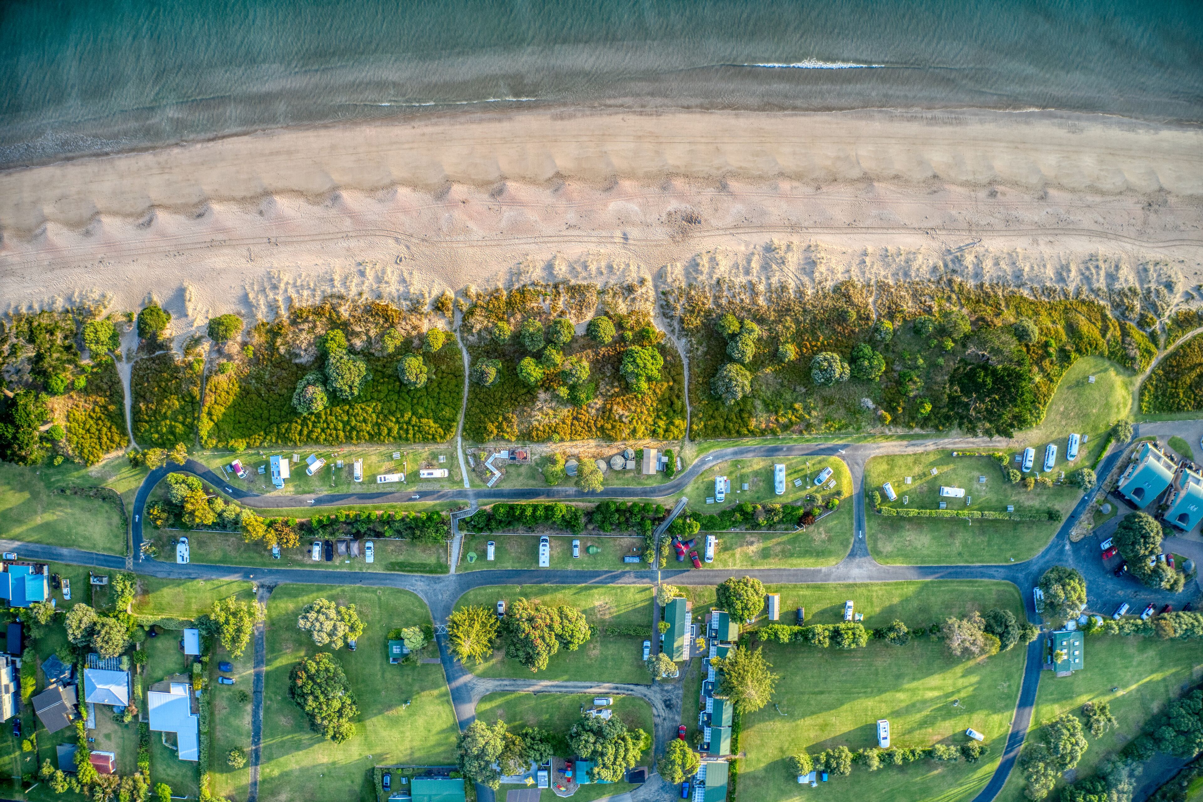 Vista aérea de una zona costera con playa, una red de carreteras y edificios dispersos.