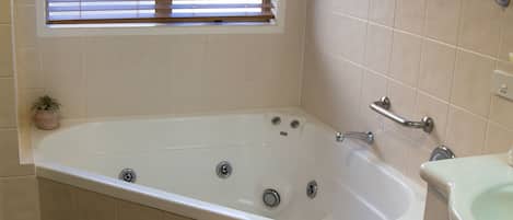 Un baño con bañera, una ventana con persianas, un perchero para toallas y un lavabo.