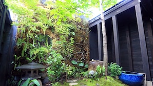 Um jardim com um lampião de pedra, chão coberto de musgo e um vaso azul grande.