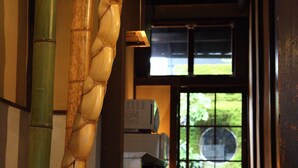 Um corredor com uma escultura de bambu, uma porta com um vitral circular e uma geladeira ao fundo.