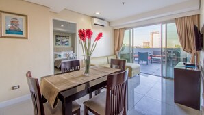 A modern dining area with a table set for four, a vase with red flowers, and a view of the cityscape through large sliding glass doors. - Alicia Apartelle (Cebu City)