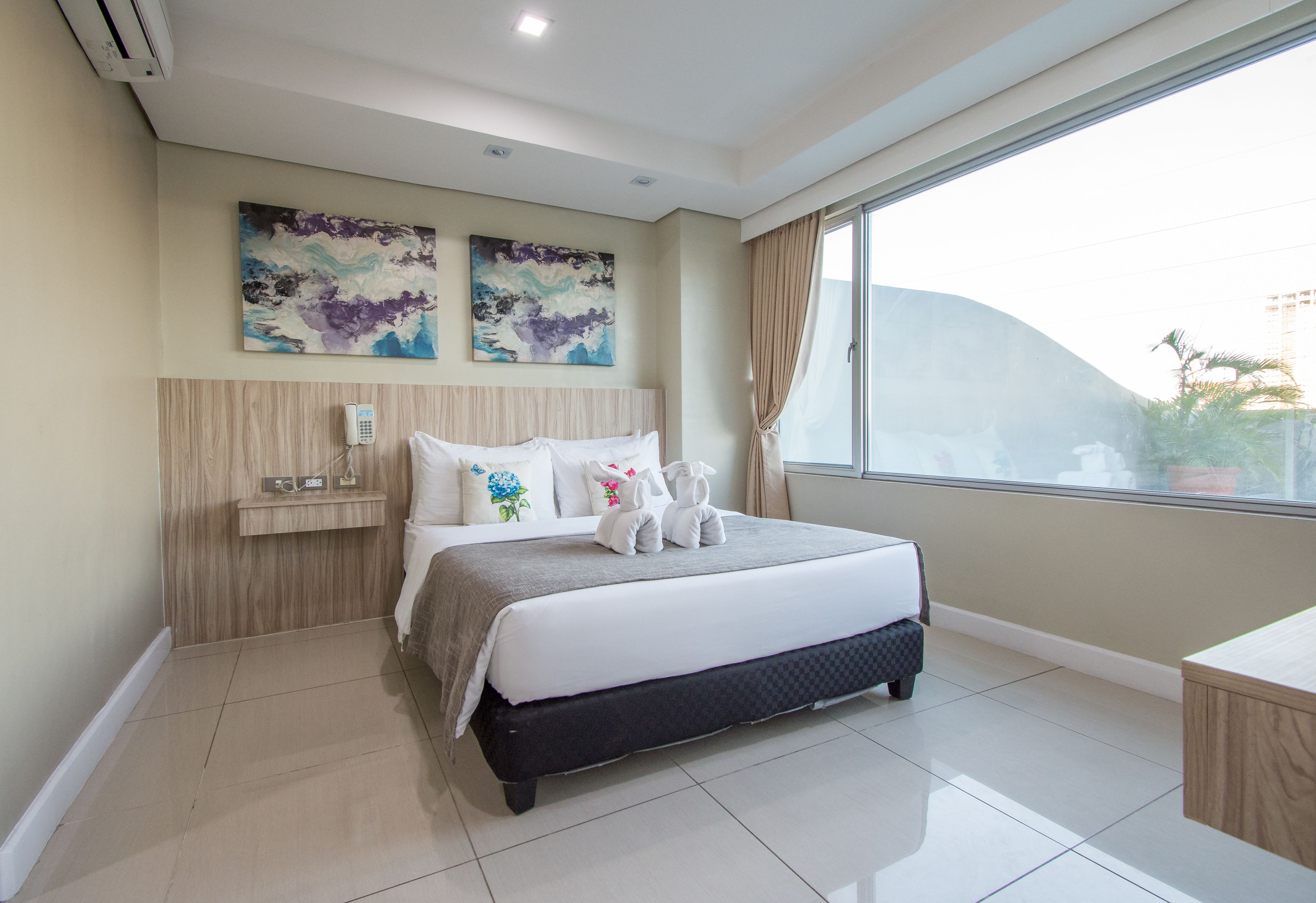A modern hotel room with a large bed, a bedside telephone, and two abstract paintings on the wall.