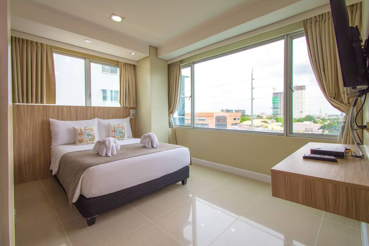 A hotel room with a bed, a desk, and a large window with curtains.