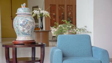 A blue armchair and a decorative vase on a wooden table in a room with a wooden cabinet and a vase of flowers.