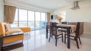 A modern living room with a sofa, dining table, chairs, and a large window offering a city view. - Alicia Apartelle (Cebu City)