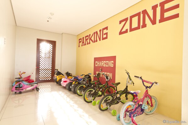 A children's play area with a row of bicycles and scooters, a charging station, and a door with a lattice design.