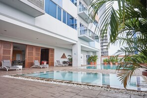 Ein Poolbereich mit Liegestühlen und einem Mehrstöckengebäude mit Balkonen.