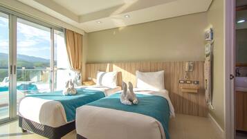 A hotel room with two beds, a large window with curtains, a wooden headboard, a bedside phone, and a view of a pool and mountains.