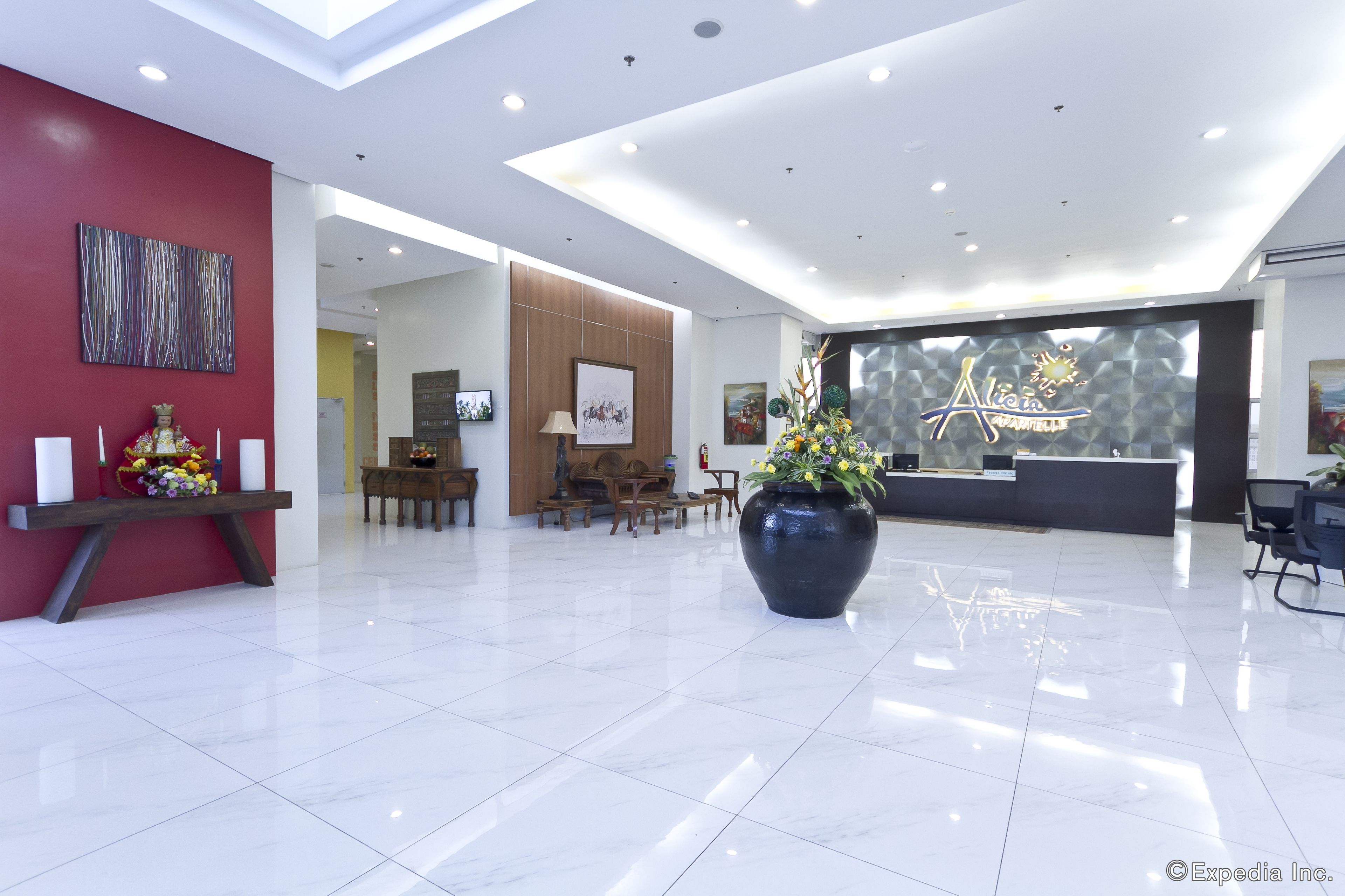 A modern hotel lobby with a reception desk, seating area, and a large vase with flowers.
