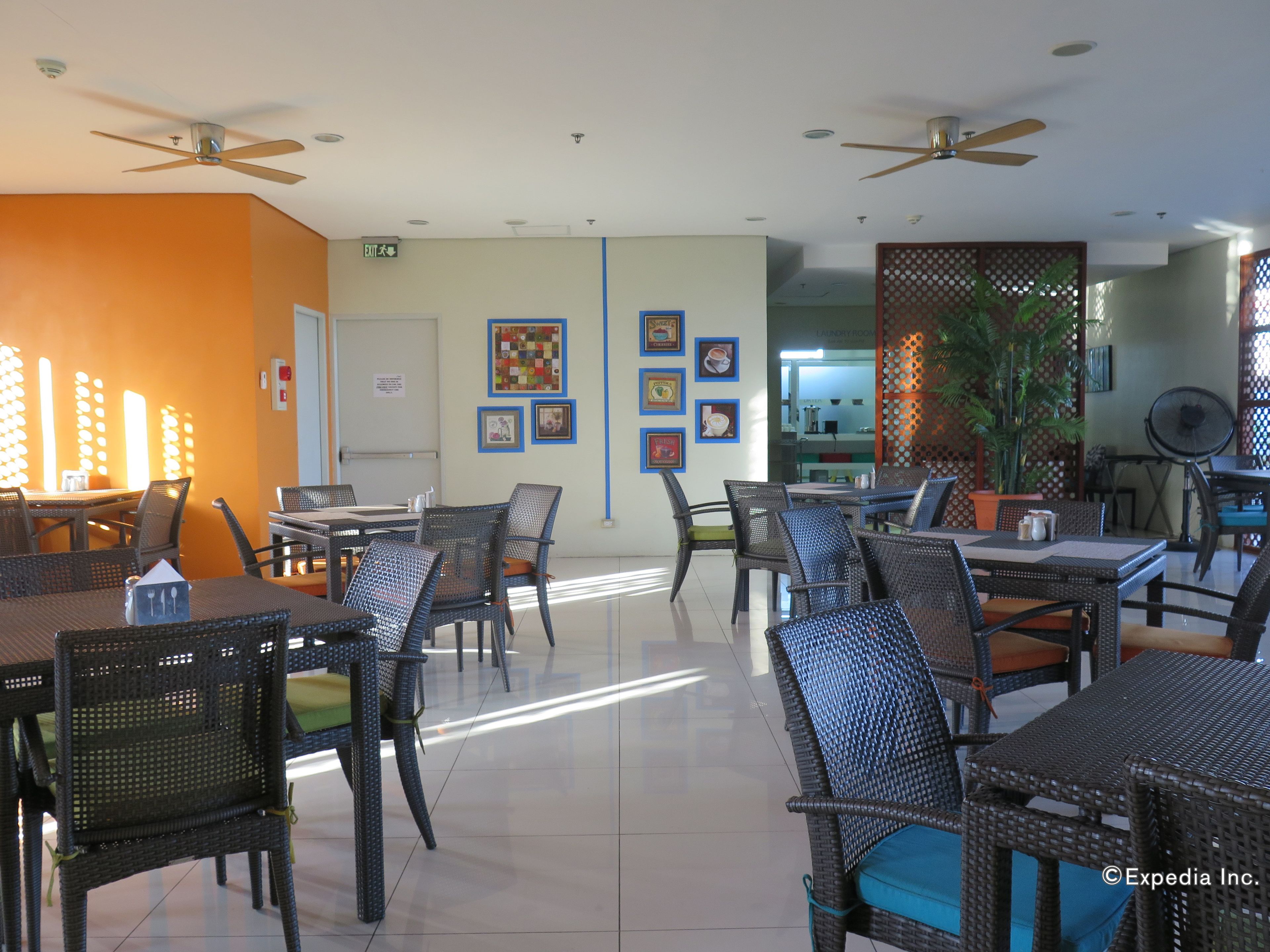 A restaurant with wicker furniture, a visible exit sign, and framed pictures on the wall.