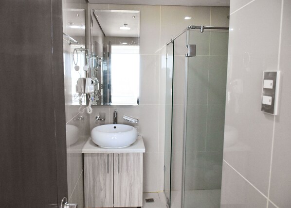 Un baño moderno con un lavabo blanco, cabina de ducha de vidrio y un espejo sobre el lavabo.