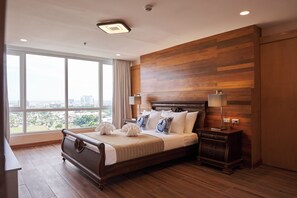Habitación de hotel con una cama grande, lámparas de noche, mesitas de noche y vistas a la ciudad a través de amplios ventanales.