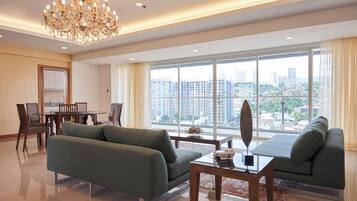 Un vaste salon agrémenté d’un lustre, un coin repas avec des chaises et une table, et de grandes fenêtres offrant une vue sur la ville.