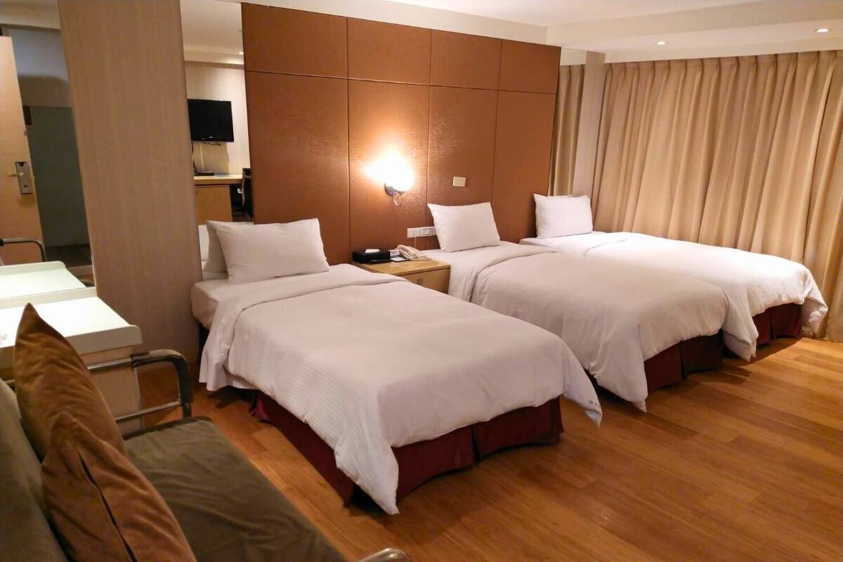 A hotel room with two beds, a desk, and a TV.