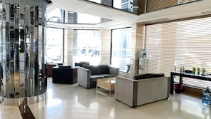 A modern lobby with a glass wall, seating area with sofas, a coffee table, and a water dispenser. - Delton Hotel (Kaohsiung)