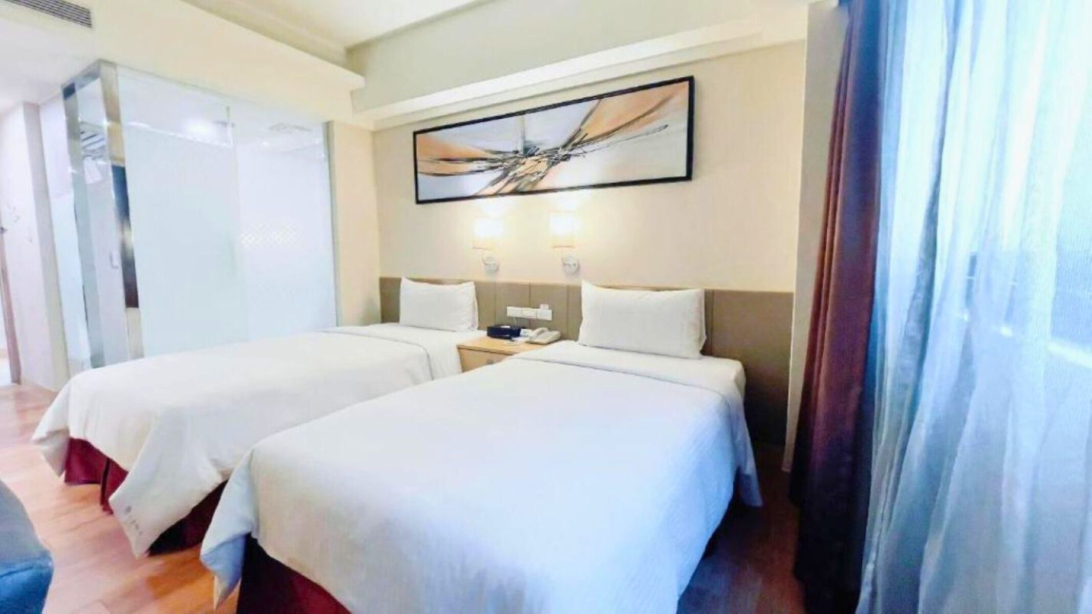A hotel room with two beds, a bedside table with a phone, and a painting on the wall.