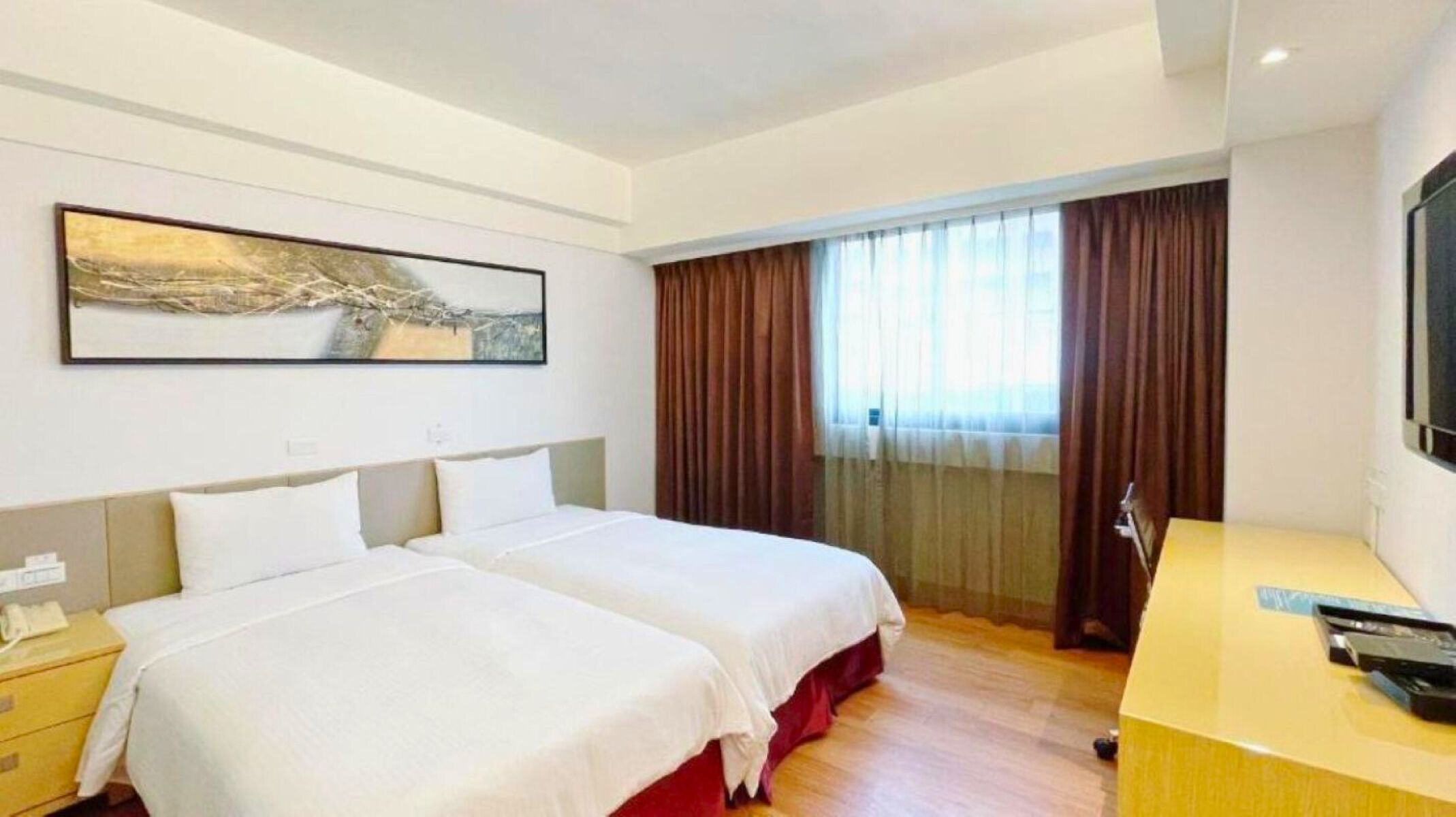Ein Hotelzimmer mit zwei Betten, einem Schreibtisch, einem Stuhl, einem Fernseher und einem Fenster mit Vorhängen.