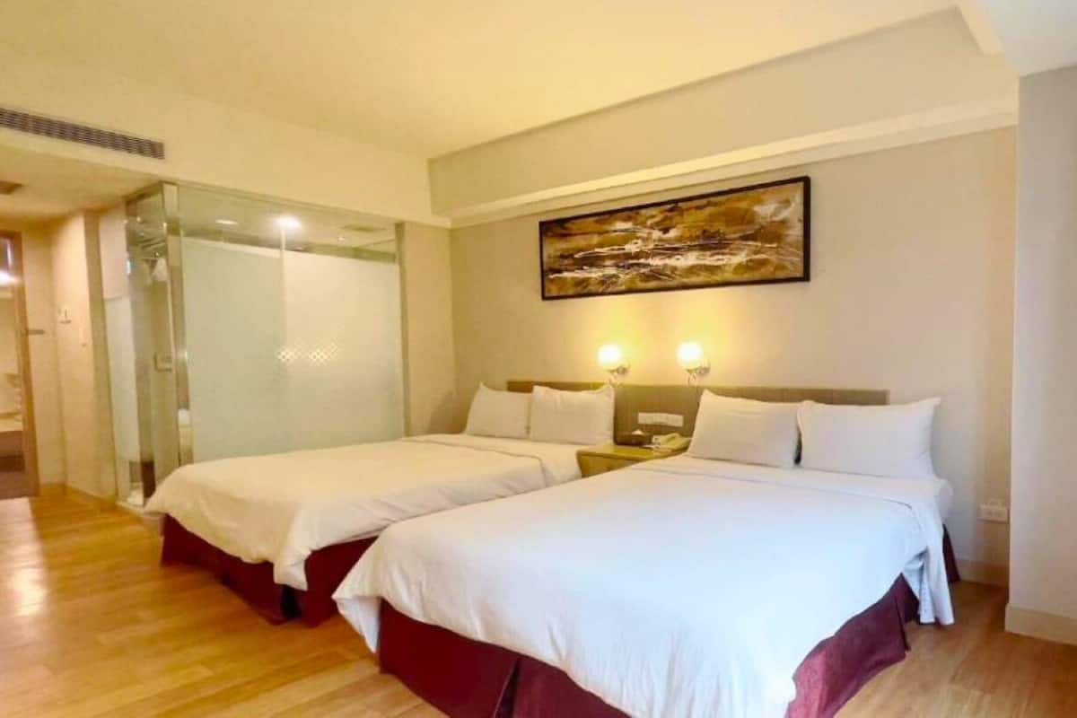 A hotel room with two beds, a glass shower enclosure, and a painting on the wall.