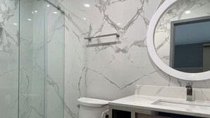 Un bagno con il water, una cabina doccia in vetro, una parete in marmo e uno specchio rotondo.