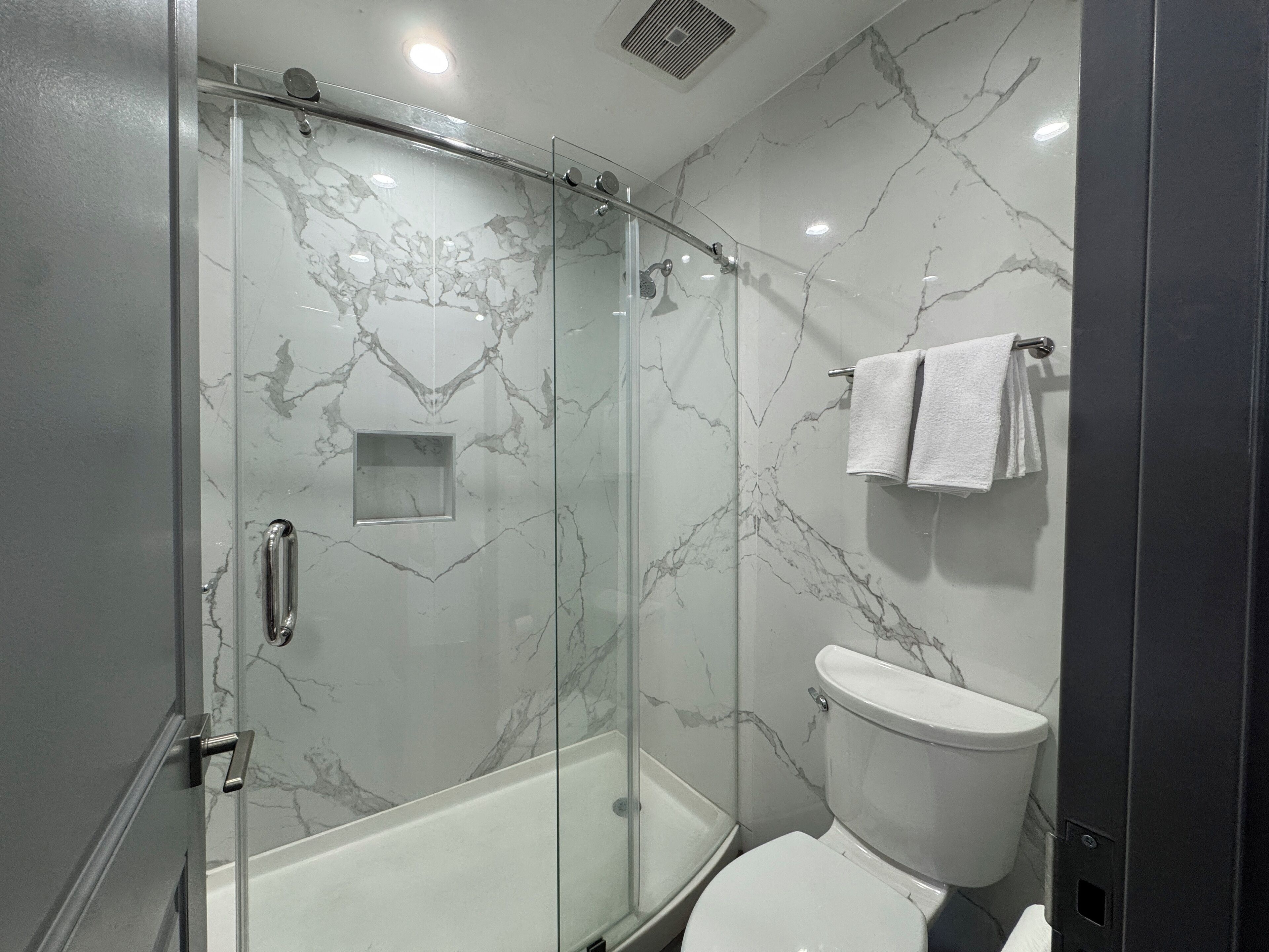 A modern bathroom with a glass-enclosed shower, a white toilet, and marble walls.