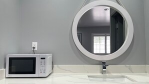 Un bagno con un lavabo, uno specchio e un forno a microonde su un ripiano bianco.