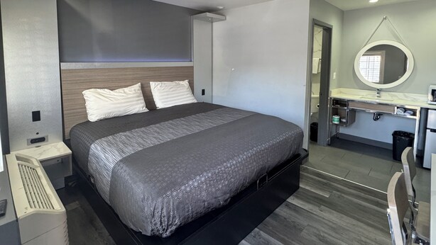 Una camera da letto moderna con un letto grande, una scrivania integrata e un bagno visibile attraverso una porta aperta.
