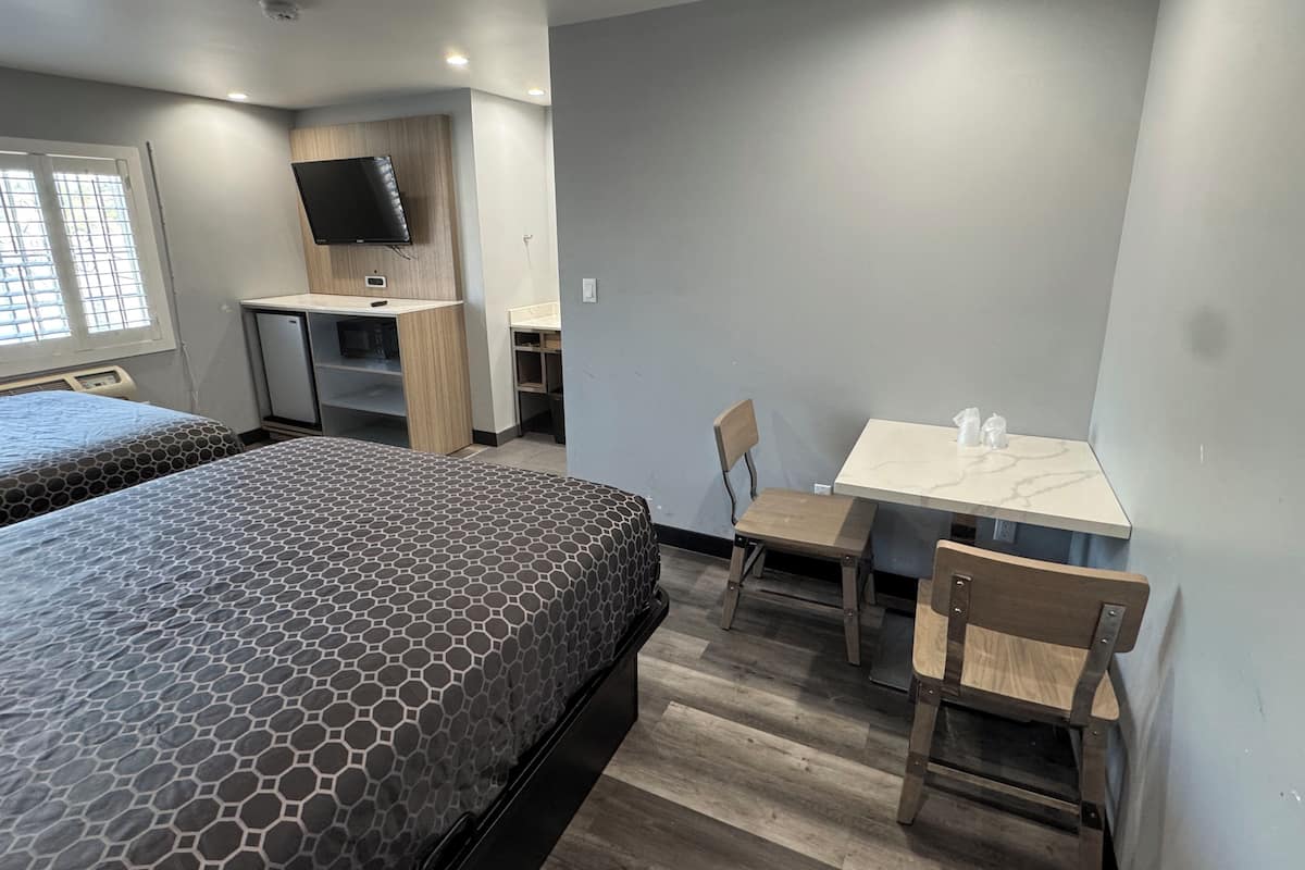 Quarto de hotel com duas camas, uma escrivaninha, uma cadeira e uma televisão.