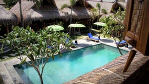 A swimming pool with lounge chairs and umbrellas, surrounded by thatched-roof huts. - The Calmtree Bungalows (Canggu)