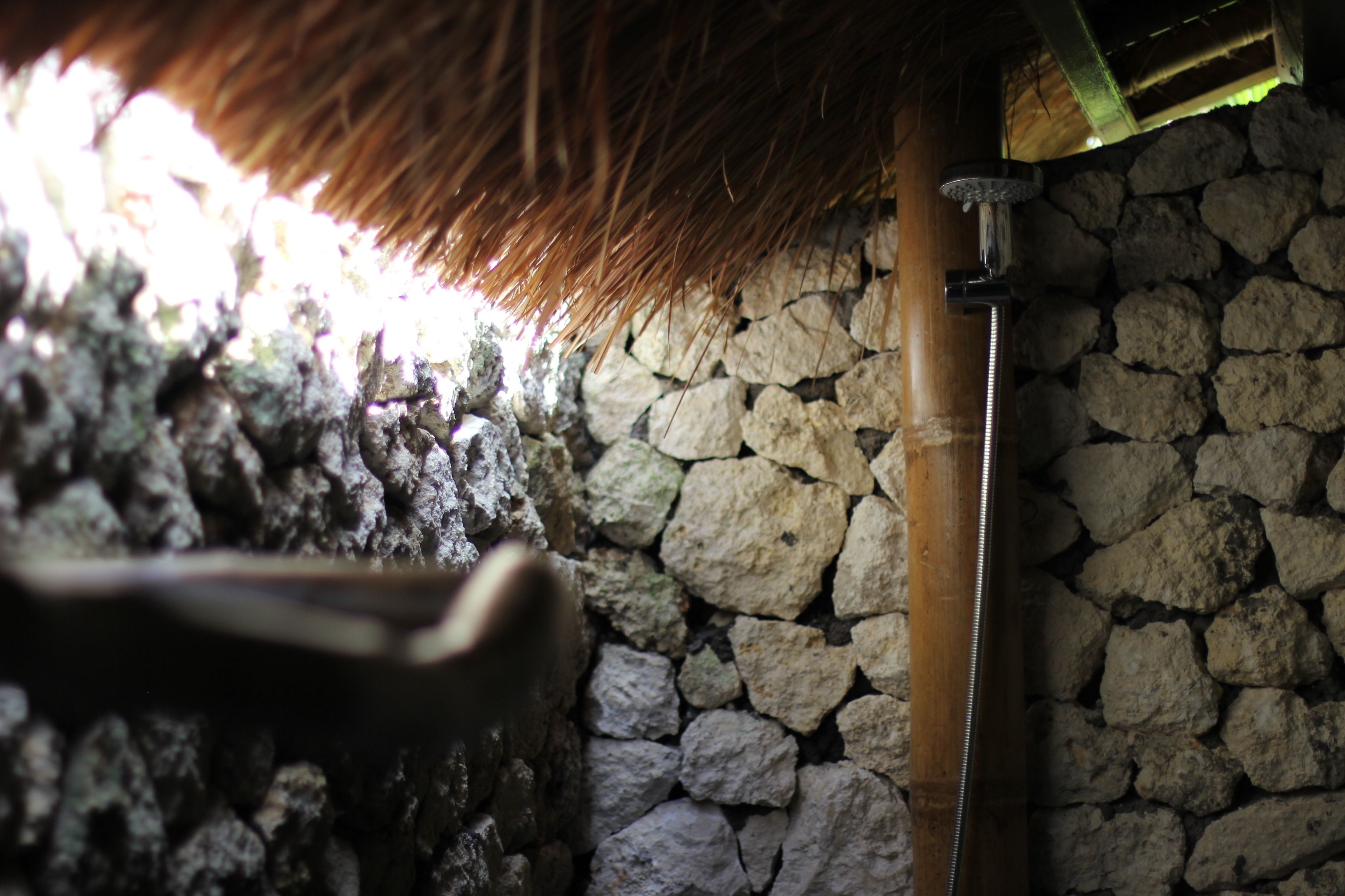 A stone wall with a thatched roof and a metal pipe.