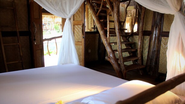 A bed with a canopy, wooden walls, and a staircase. - The Calmtree Bungalows (Canggu)