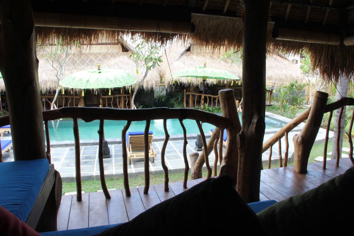 A wooden deck with a pool, thatched umbrellas, and lounge chairs.