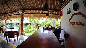 A restaurant with a thatched roof, a pool, and a 'Happy Holidays' sign. - The Calmtree Bungalows (Canggu)