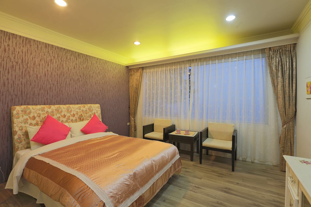 Una habitación de hotel con una cama grande, dos sillas, una mesita y una ventana con cortinas.
