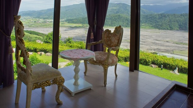 A room with a large window offering a view of a lush valley and mountains. Inside, there is a white table with a floral tablecloth and two ornate chairs. - Hao Wang Jiao Homestay (Datong)