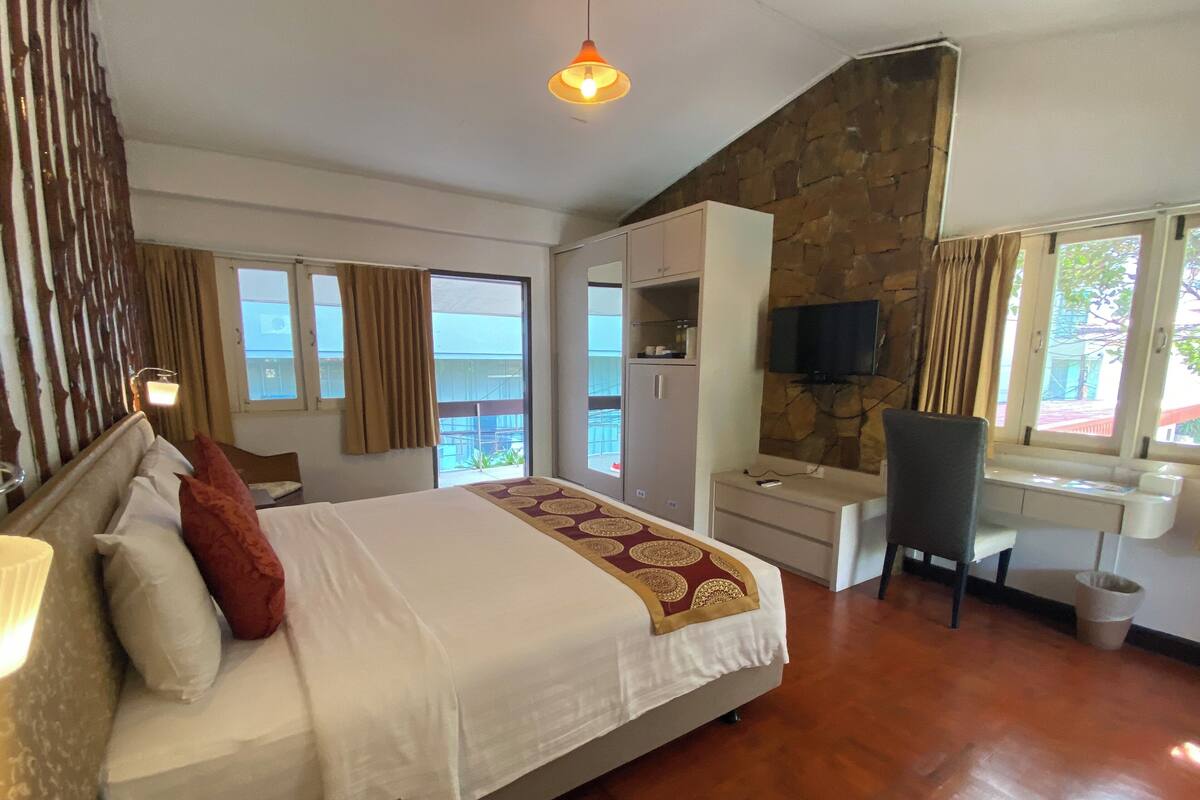 Una camera d'albergo con un letto, una scrivania, una sedia, una televisione e un muro in pietra.