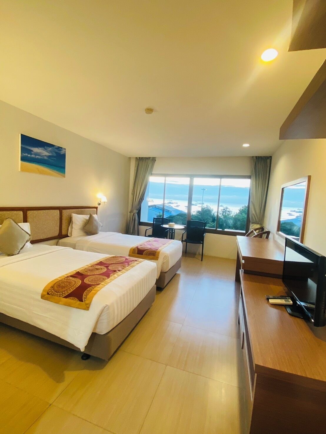 Camera d'albergo con due letti, una scrivania, una TV e vista sul mare.