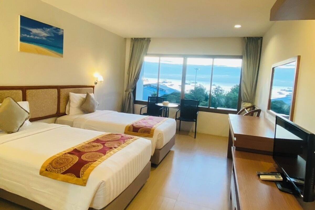 Una camera d'albergo con due letti, una scrivania, una televisione e vista sul mare.