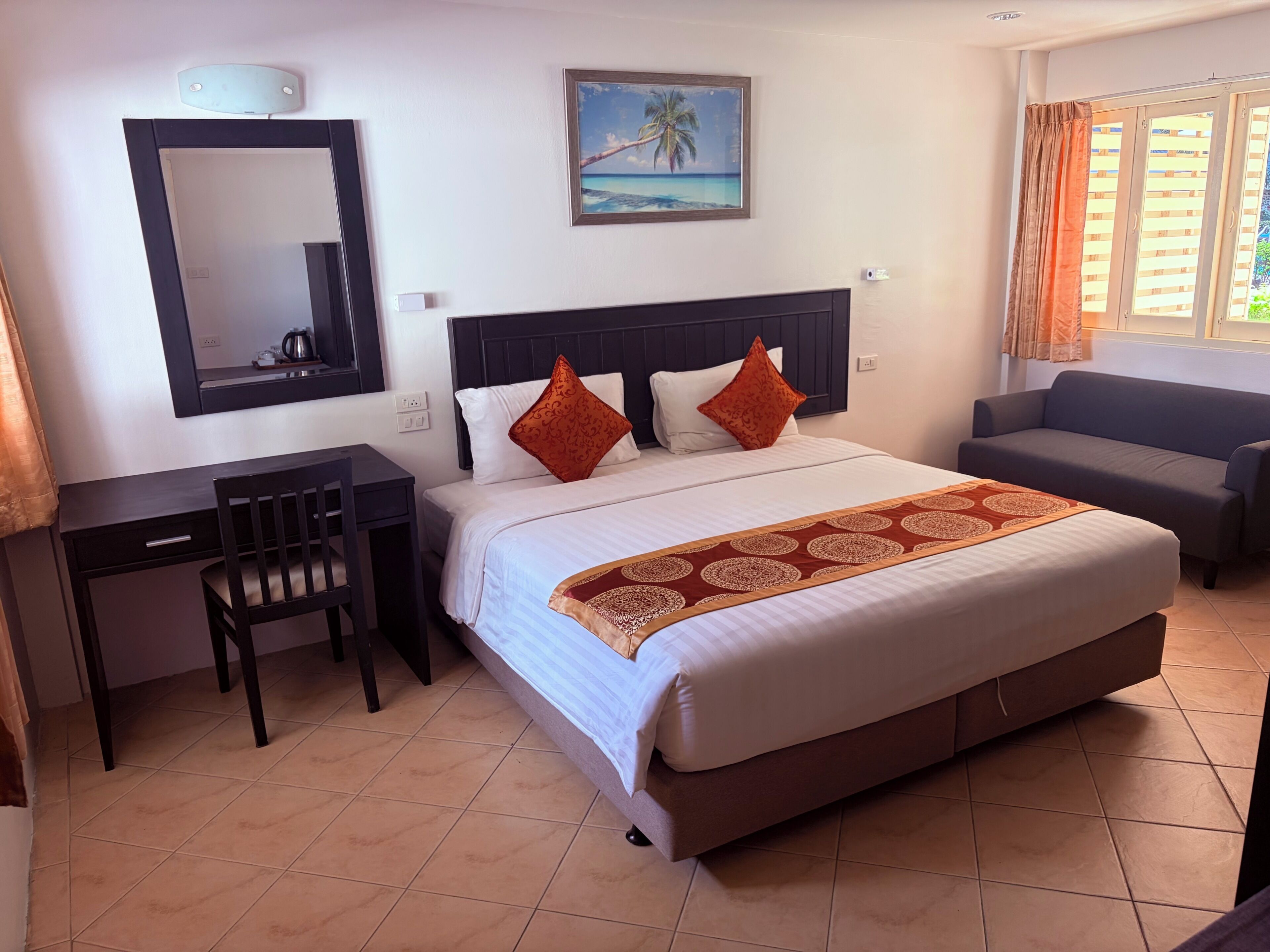 Una camera d'albergo con un letto, una scrivania, una sedia, un divano, un quadro e una finestra con tende.