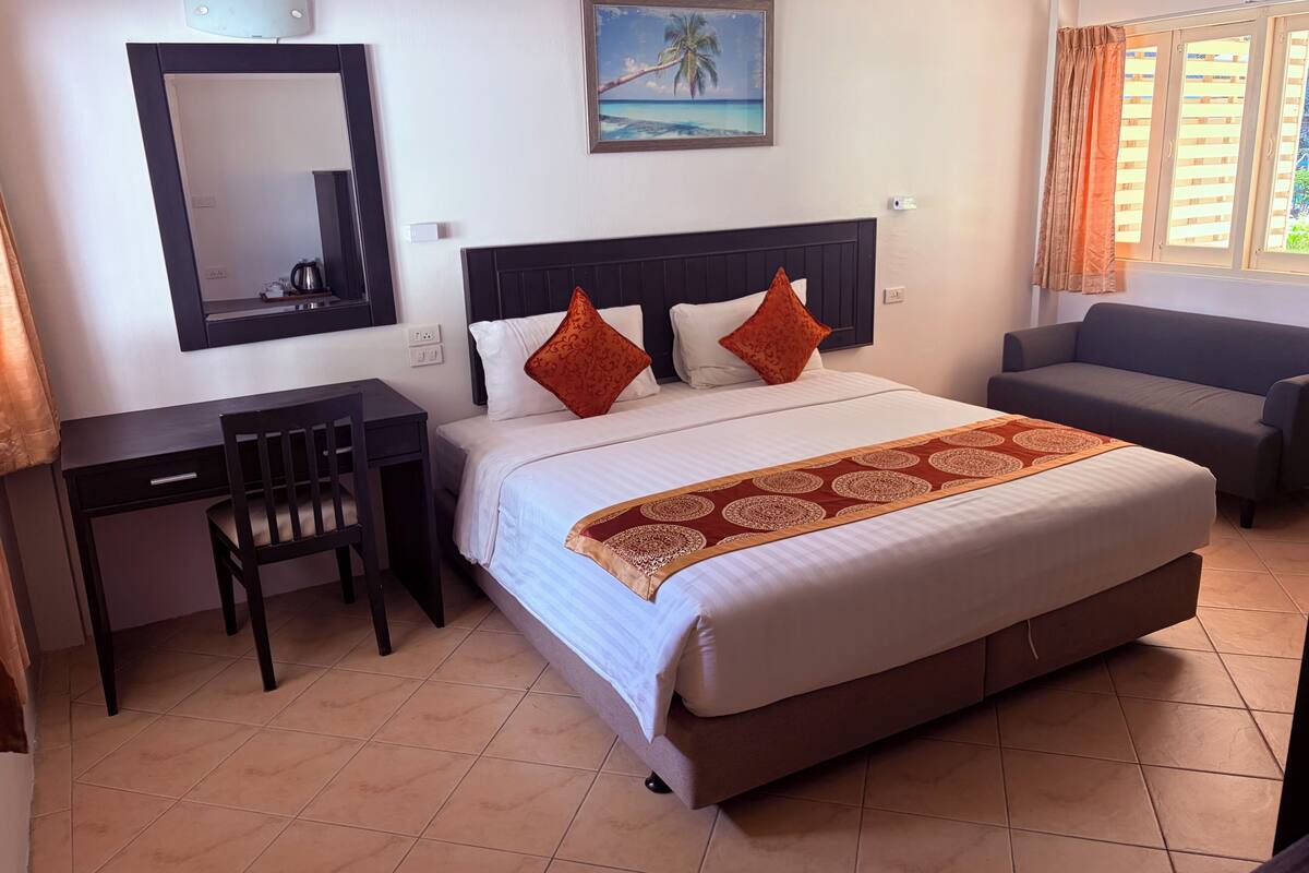 Una camera d'albergo con un letto, una scrivania, una sedia, un divano, un quadro e una finestra con tende.