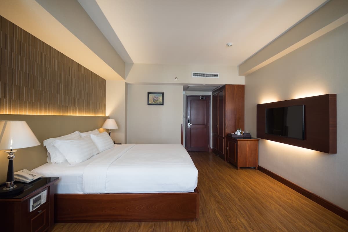 A hotel room with a large bed, bedside lamps, a flat-screen TV mounted on the wall, and a wooden floor.