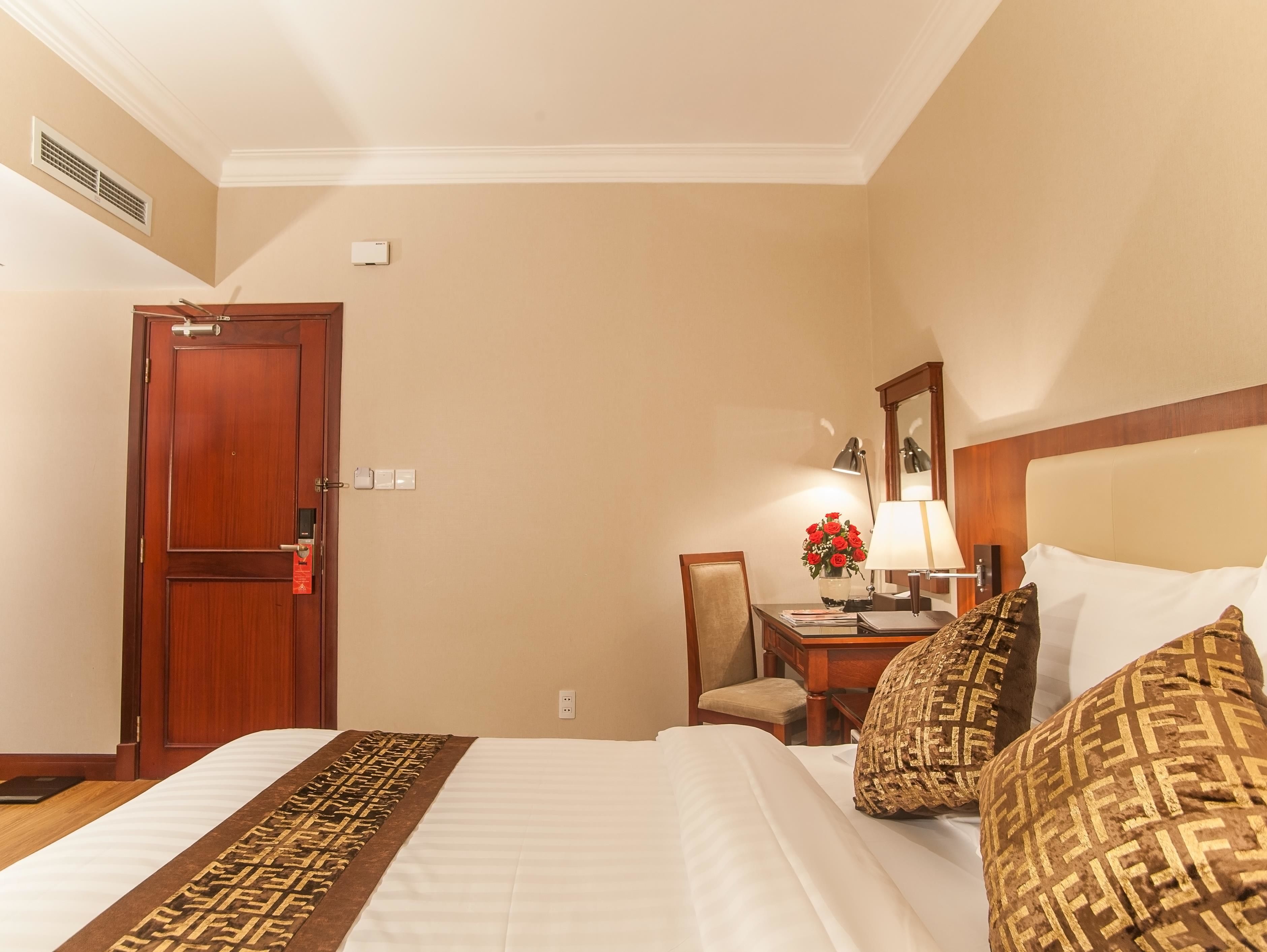 Habitación de hotel con cama, escritorio con lámpara, silla y una mesita con un florero.